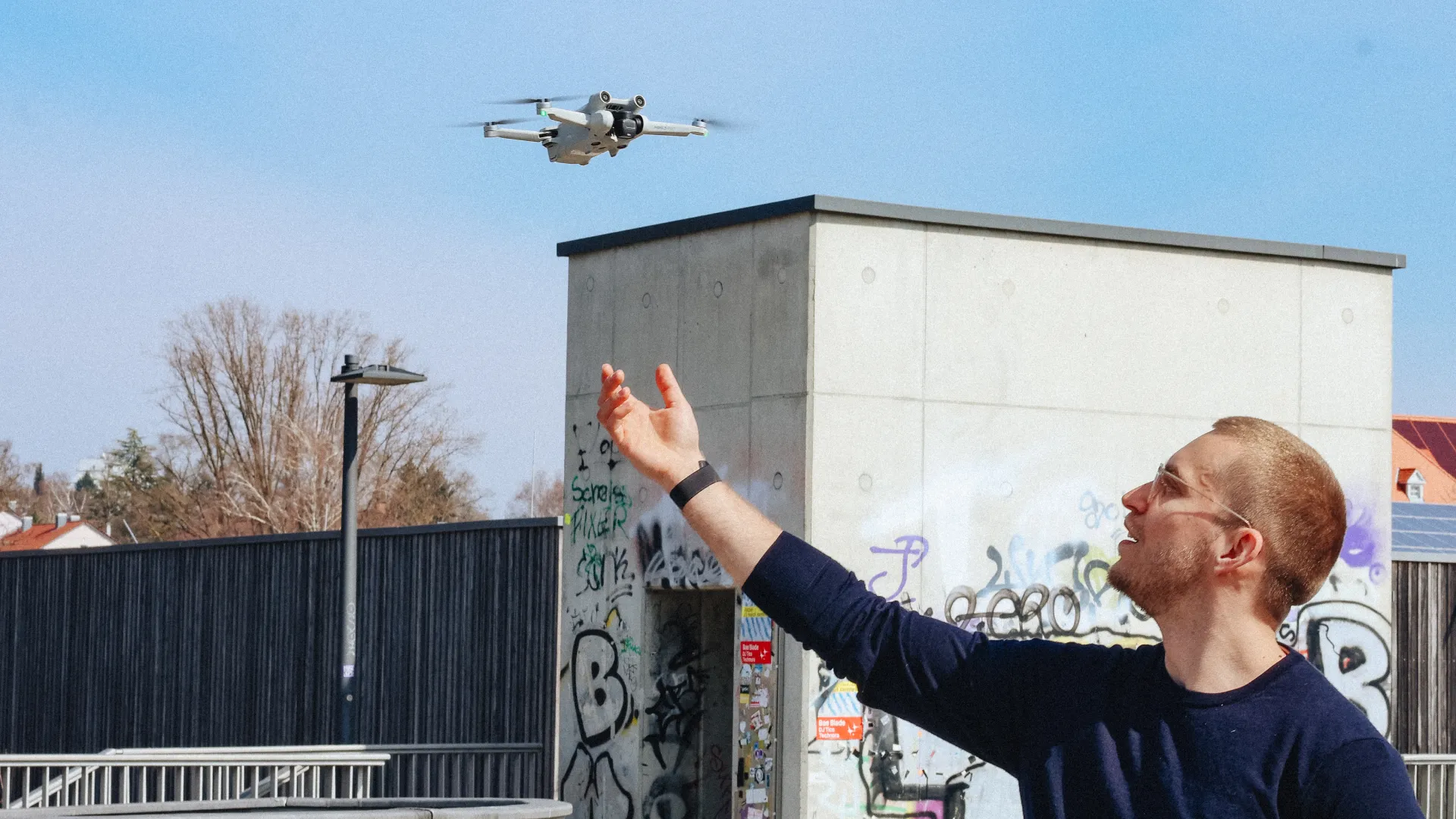 Mann mit ausgestreckter Hand neben einer fliegenden Drohne vor einem Gebäude.
