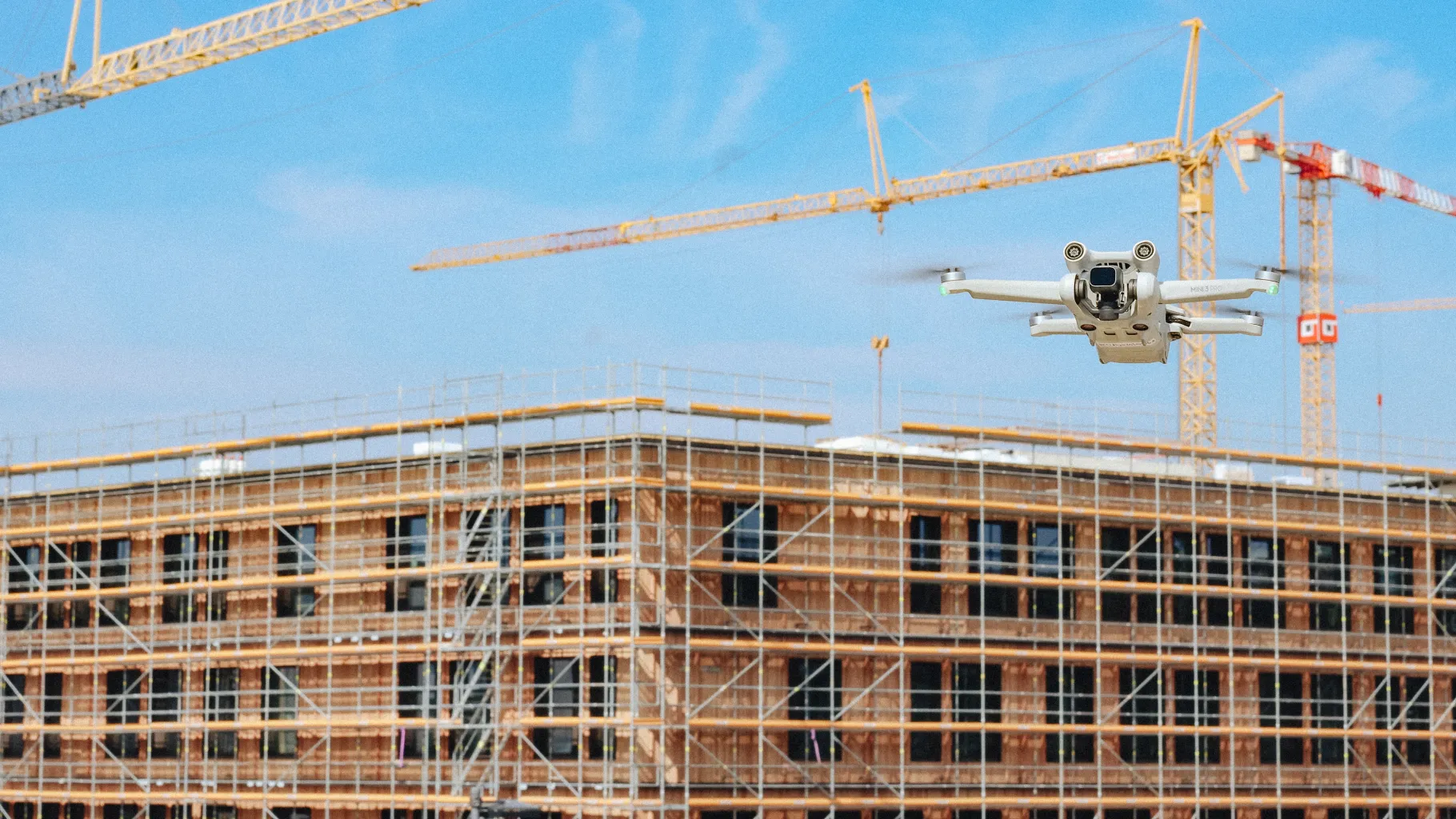 Drohne vor einem Rohbau mit Gerüsten und Baukränen.
